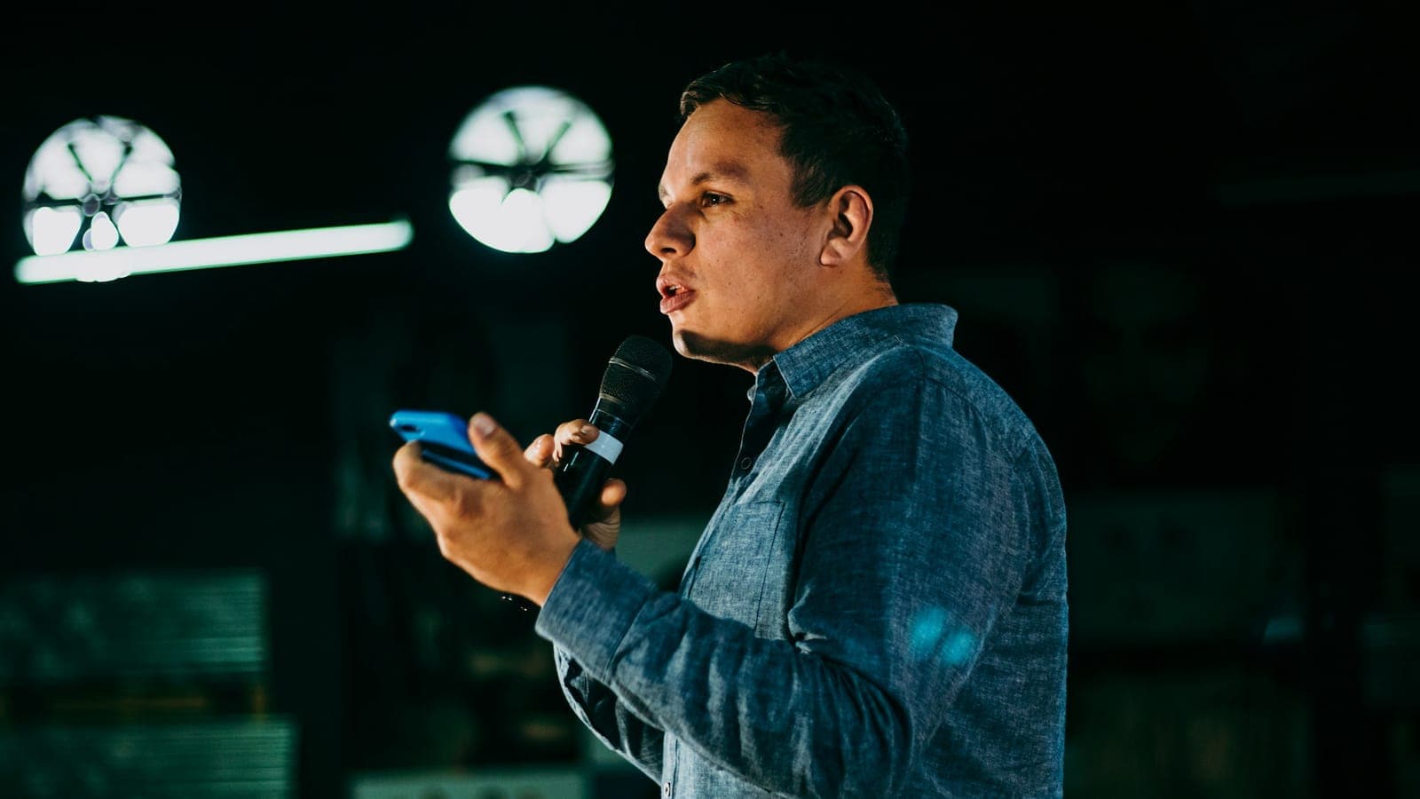 A man speaks into a handheld microphone, holding a phone in his other hand.